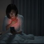 夜中に胸やけで苦しみ、スマートフォンで逆流性食道炎について検索する女性。